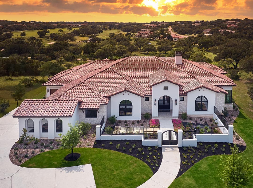 White stucco home with a terracotta tile roof and landscaped garden at sunset